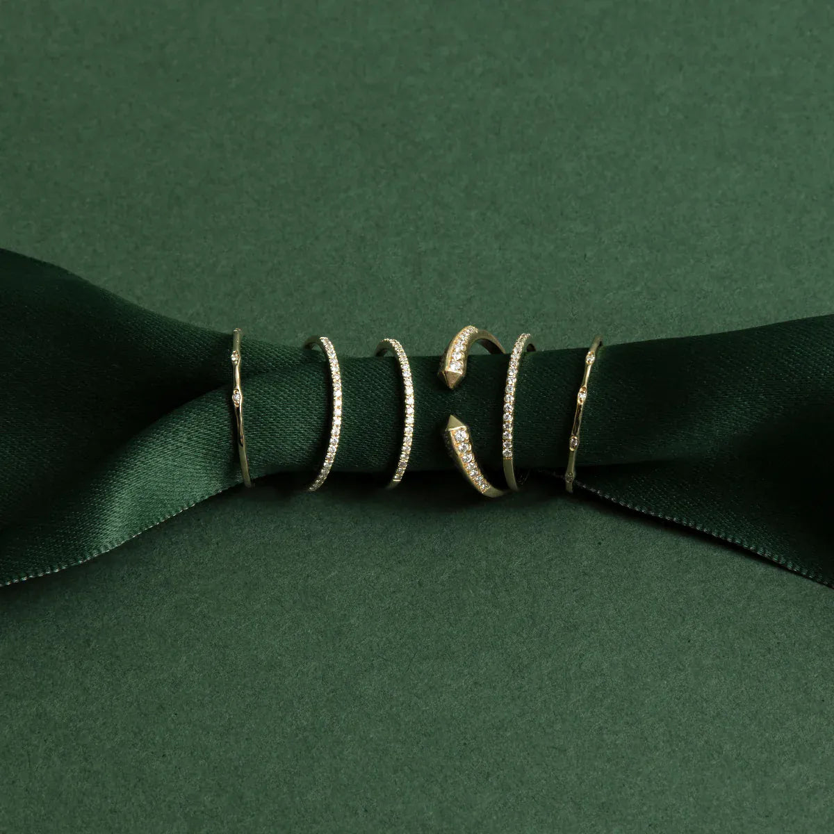 Two 4 Diamond Rings, three Pave Diamond Rings and an Open Diamond Ring on a dark green ribbon against a green background. 
