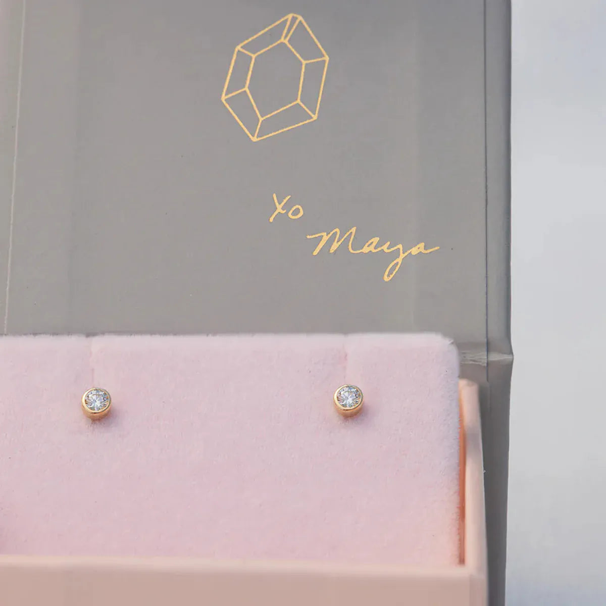 A pair of Birthstone Studs - Diamond (April) in a Maya Brenner jewellery box against a light grey background. 
