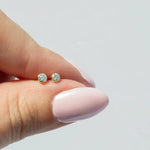 A hand holding a pair of Birthstone Studs - Diamond (April) against a light grey background. 