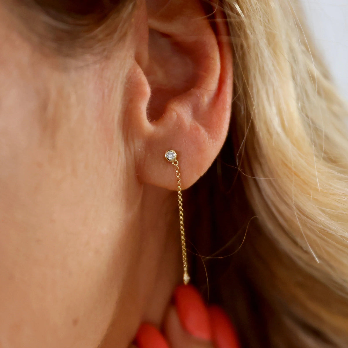Close-up of a yellow gold Droplet Diamond Earring in a blonde woman's ear. 