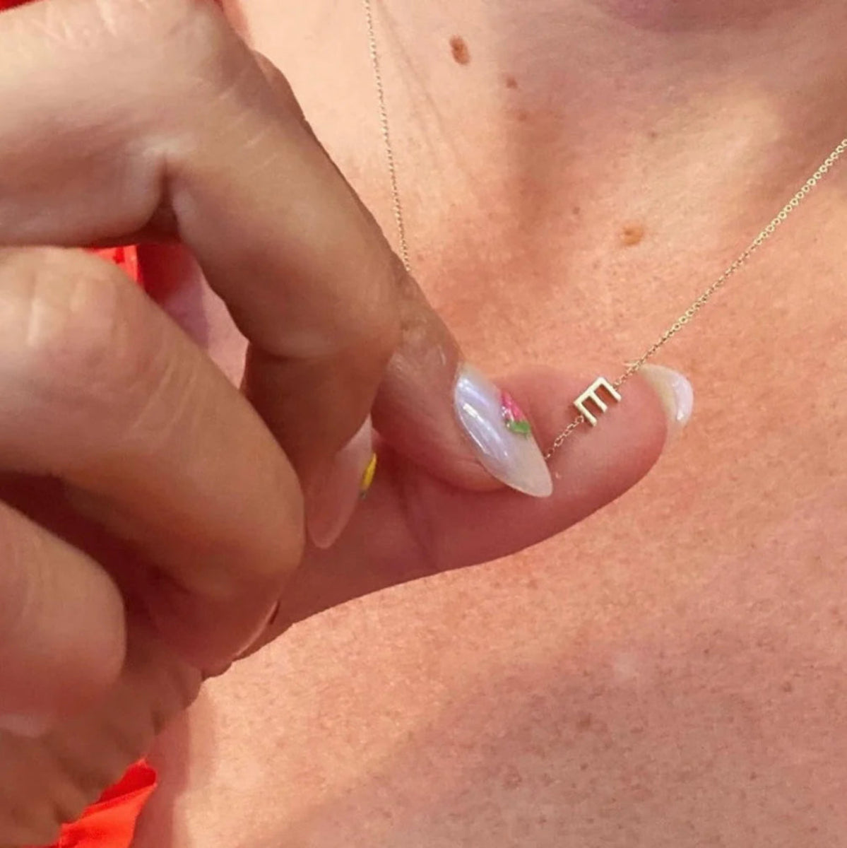 Close-up of a hand with a gold necklace featuring a letter E charm. 