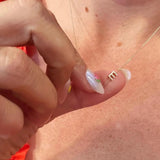 Close-up of a hand with a gold necklace featuring a letter E charm. 