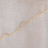 A yellow gold necklace with a letter E charm, displayed diagonally on a cream fabric background.