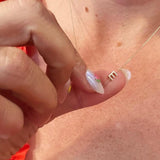 Close-up of a hand with a gold necklace featuring a letter E charm.