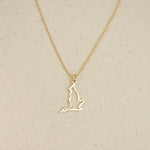 An England pendant necklace in yellow gold with a beaded chain on a beige fabric background. 