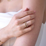 A woman's hand wearing The Magnolia Bouquet Ring and The Evermore Ring, with a white strapless top. 