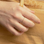 Close-up of a hand wearing a 4 Diamond Ring, holding onto yellow denim pants. 