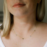 Close up of a  woman's neck wearing a 5 of Hearts Necklace in yellow gold with a white top and her blonde hair partially visible. 