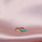 An Alli Webb Opal Huggie and Turquoise Huggie on a light pink silk fabric. 