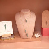 Three Protection Retreat Necklaces on a neck mannequin and a Courage Retreat Necklace on a smaller pink stand, with a Labradorite Protection Necklace note on a small paper, all set against a pink background.