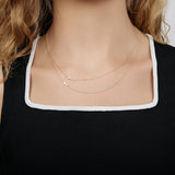 A close-up of a person's neck wearing two 14k Gold Asymmetrical Charm Necklaces in Cross and Pavé Cross, both in yellow gold, styled with a black and white top.