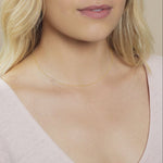 Close-up of a woman's neck wearing a gold necklace with a letter G charm.