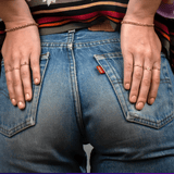 Close-up of a person wearing blue jeans with their hands on the back pockets, wearing gold rings and bracelets including two Diamond Cut Bracelets, a Rolo Bracelet and various Letter Rings.