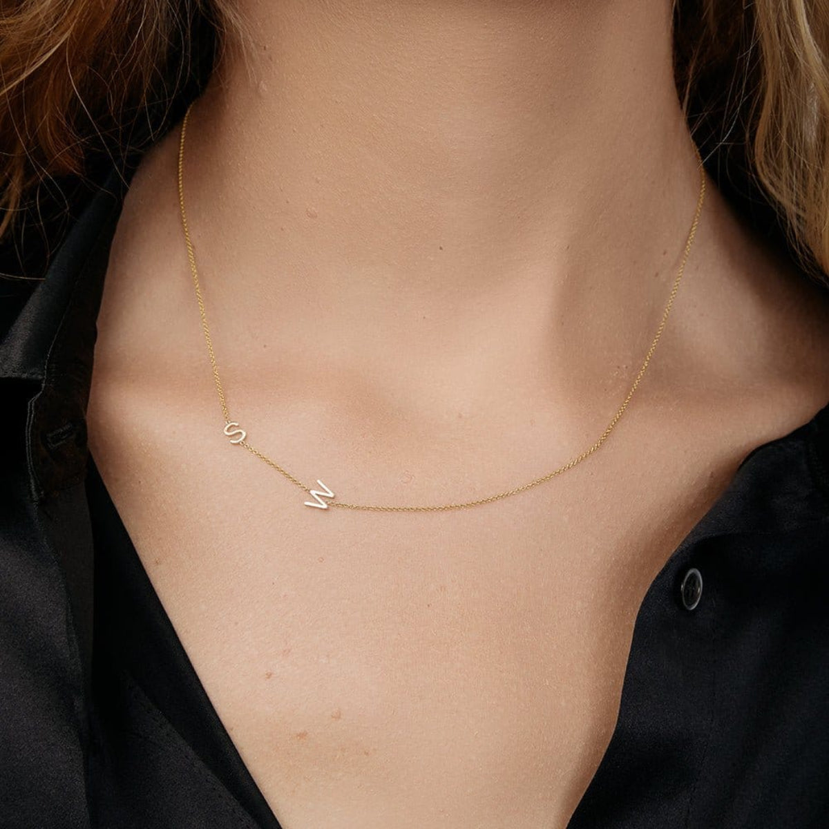 A close-up of a woman’s neck wearing a Custom Gold Necklace in yellow gold with the letters S and W, and a black shirt. 