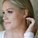 A blonde woman wearing a Lip Stud and a 
Thin Gold Hoop with a white top and blurred background. 