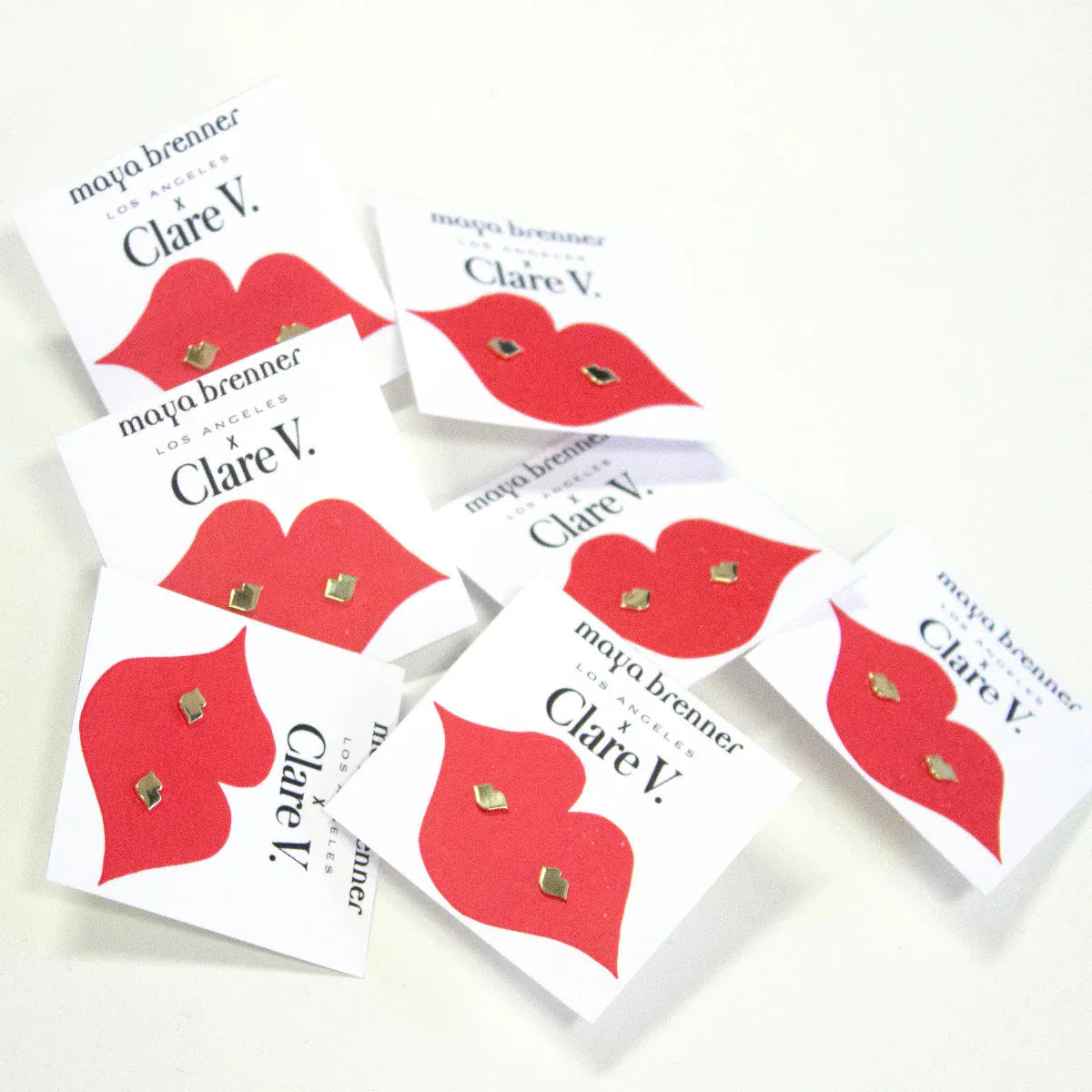 Various Lip Studs on white cards with Maya Brenner x Clare V and red lips against an off-white background. 