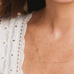 A close-up of a woman’s chest and neck area in a white embroidered top wearing a Monogram Necklace with Heart Yellow Gold and a letter D charm.