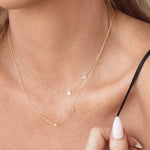 A close-up of a woman’s neck wearing a Monogram Necklace with Heart and the letter K and a Monogram Necklace with Diamond and the letter R, both in yellow gold.