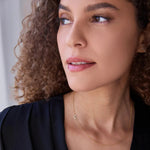 A woman wearing a yellow gold 14k Gold Asymmetrical Charm Necklace - Pavé Moon, with curly hair, styled in a navy top. 

