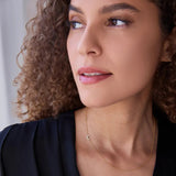 A woman wearing a yellow gold 14k Gold Asymmetrical Charm Necklace - Pavé Moon, with curly hair, styled in a navy top. 

