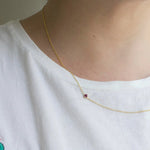 A close-up of a a neck wearing a yellow gold 14K Gold Asymmetrical Birthstone Necklace - Pink Tourmaline (October), styled in a white t-shirt. 