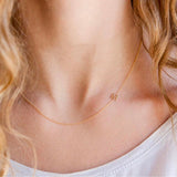 A close-up of a woman's neck wearing a yellow gold necklace with a letter M charm.