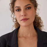 A woman wearing a yellow gold 14k Gold Asymmetrical Charm Necklace - Pavé Hamsa with a cable chain styled  which a black blazer against a white background. 

