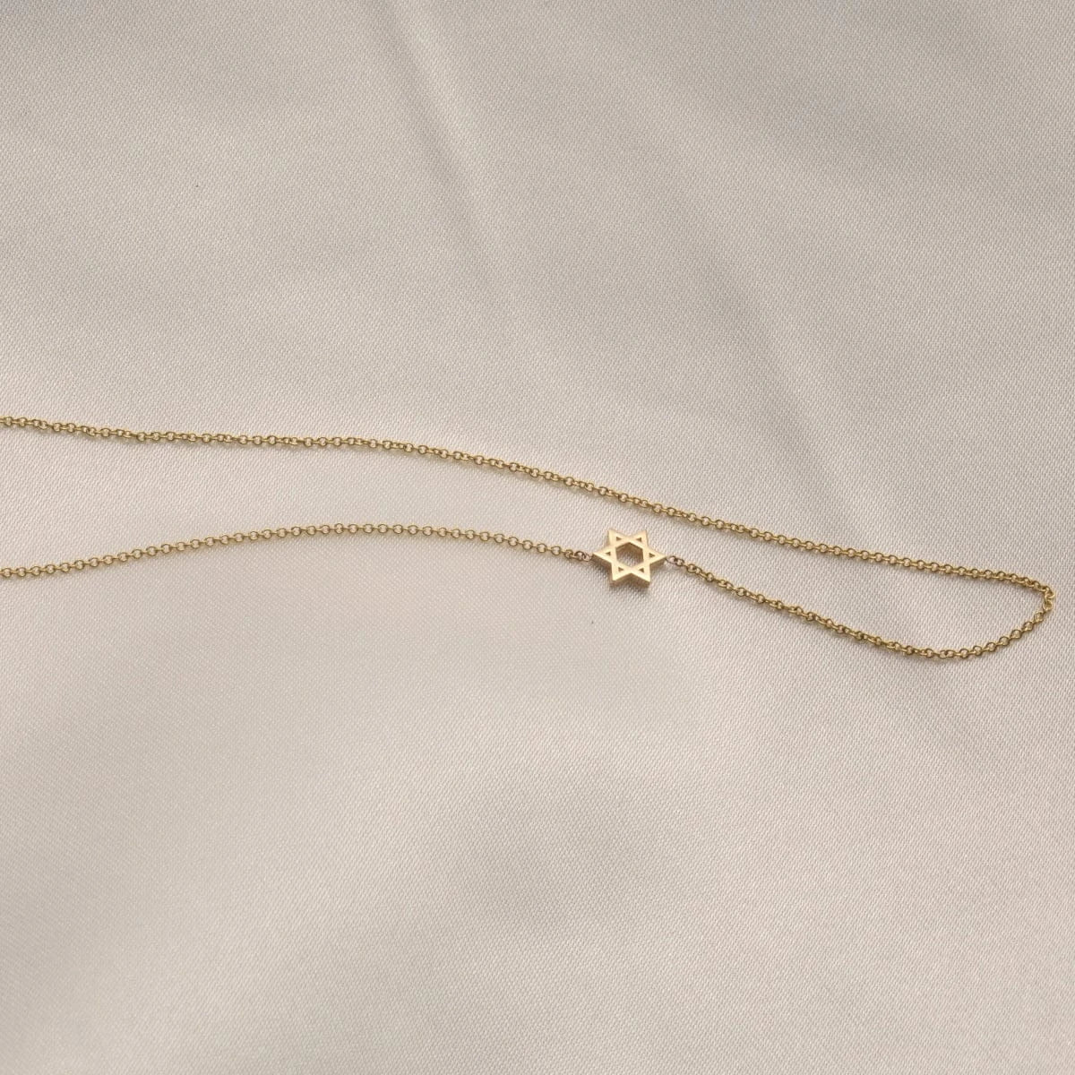 A yellow gold cable chain 14k Gold Asymmetrical Charm Necklace - Star of David against a light grey fabric background.