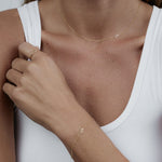 Close-up of a person a woman's decellotage and hand wearing a yellow gold 14k Gold Asymmetrical Number - 5,  Lucky Number Ring - 1, and a Custom Gold Bracelet - 1 Letter with a number 5, styled in a white tank top.