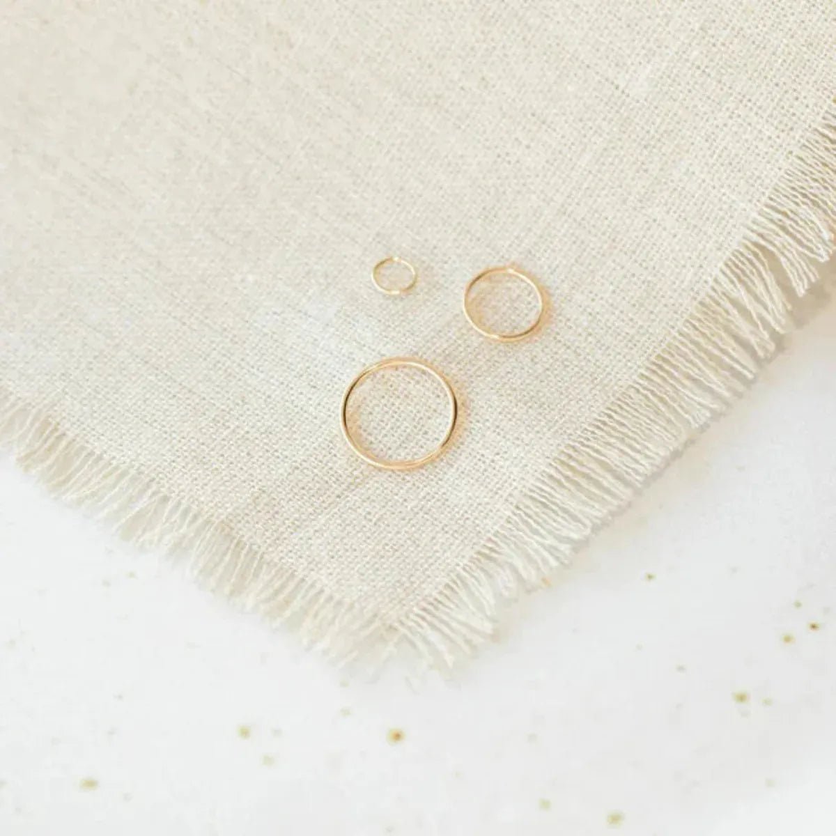 Open Eclipse Earrings (mini, small, and large) in yellow gold on a cream fabric and white speckled surface.