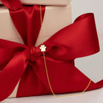 A yellow gold 14k Gold Asymmetrical Charm Necklace - Paw with a cable chain on a wrapped gift with a big red bow. 