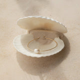 A Baroque White Pearl Bangle in a white shell on a beige background. 