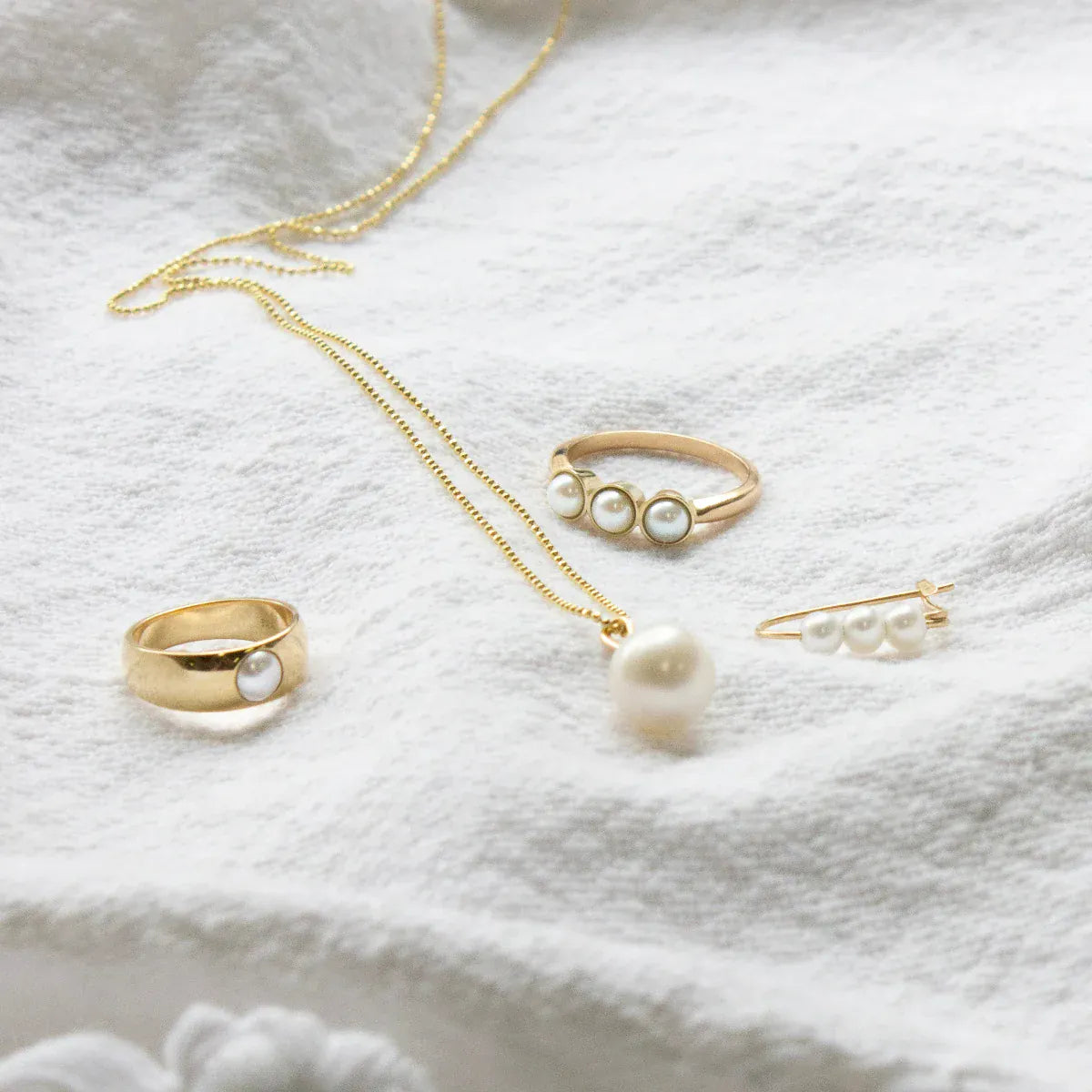 A Tres Pearl Ring, Perla Ring, Perla Necklace and a Tres Pearl Earring on white fabric. 