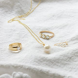 A Tres Pearl Ring, Perla Ring, Perla Necklace and a Tres Pearl Earring on white fabric. 