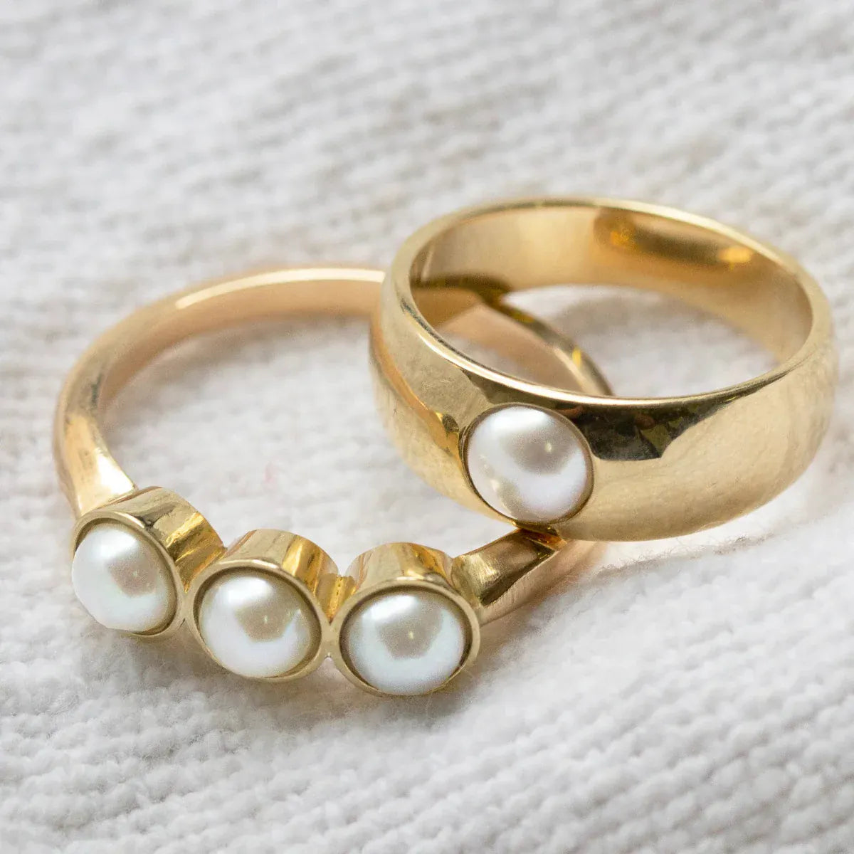 A Tres Pearl Ring and a Perla Ring on  a cream fabric background. 