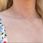 A close-up of a woman's neck wearing a gold necklace with a letter H charm.