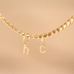 A yellow gold necklace with Petite Letter Charms in h and c on against a beige background.