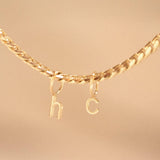 A yellow gold necklace with Petite Letter Charms in h and c on against a beige background.
