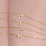 Four Petite Nameplate Necklaces in yellow gold, in the names Josie, Tay, Chloe and April (all in lowercase) on a pink fabric background. 