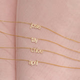 Four Petite Nameplate Necklaces in yellow gold, in the names Josie, Tay, Chloe and April (all in lowercase) on a pink fabric background. 