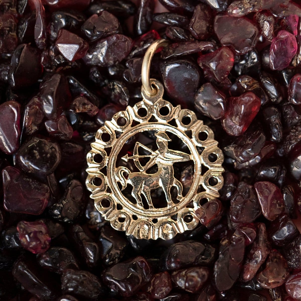 The Zodiac Necklace - Sagittarius pendant laid on top of dark red stones. 