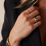 A woman’s hand wearing two 4 Diamond Rings, a Thick Band, a Delicate Band, Bubble Bracelets, a Diamond Cut Bracelet, and an Element Long Link Chain, all in yellow gold, styled with a black blazer against a light grey background.