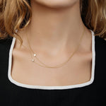 A close-up of a woman's neck wearing two yellow gold 14k Gold Asymmetrical Charm Necklaces (one star and one pavé star), styled with a black and white top. 