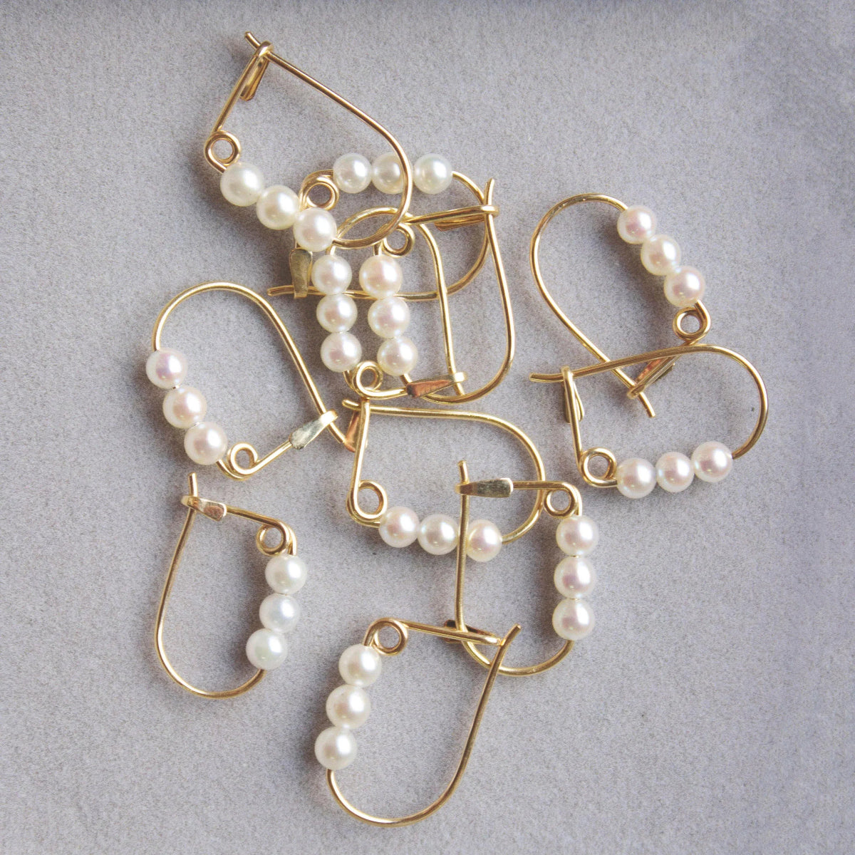 Several Tres Pearl Earrings against a light grey background. 