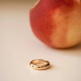A yellow gold Tube Ring with a peach in the background. 