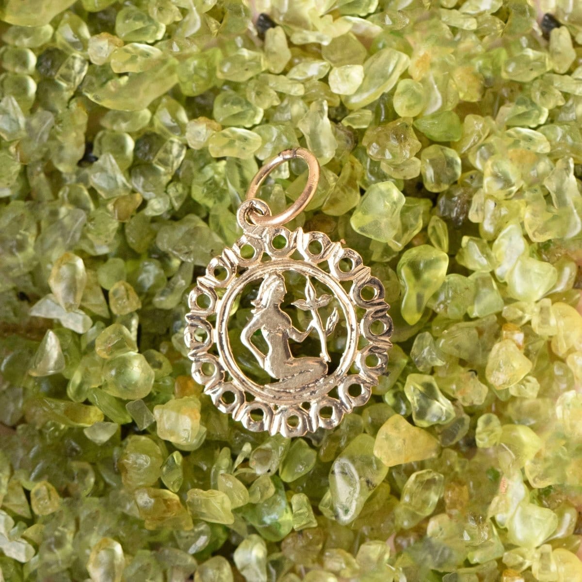 The Zodiac Necklace - Virgo pendant laid on top of green clear stones. 
