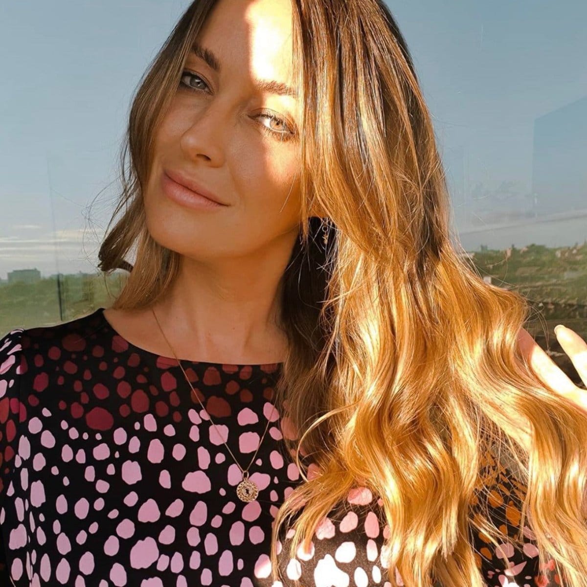 Fran Newman Young wearing a Pisces zodiac necklace, paired with a black top featuring pink and dark red spots, set against an outdoor background.