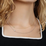 A close-up of a woman's neck wearing two 14k Gold Asymmetrical Charm Necklaces (one star in yellow gold and one pavé star in white gold), styled with a black and white top.