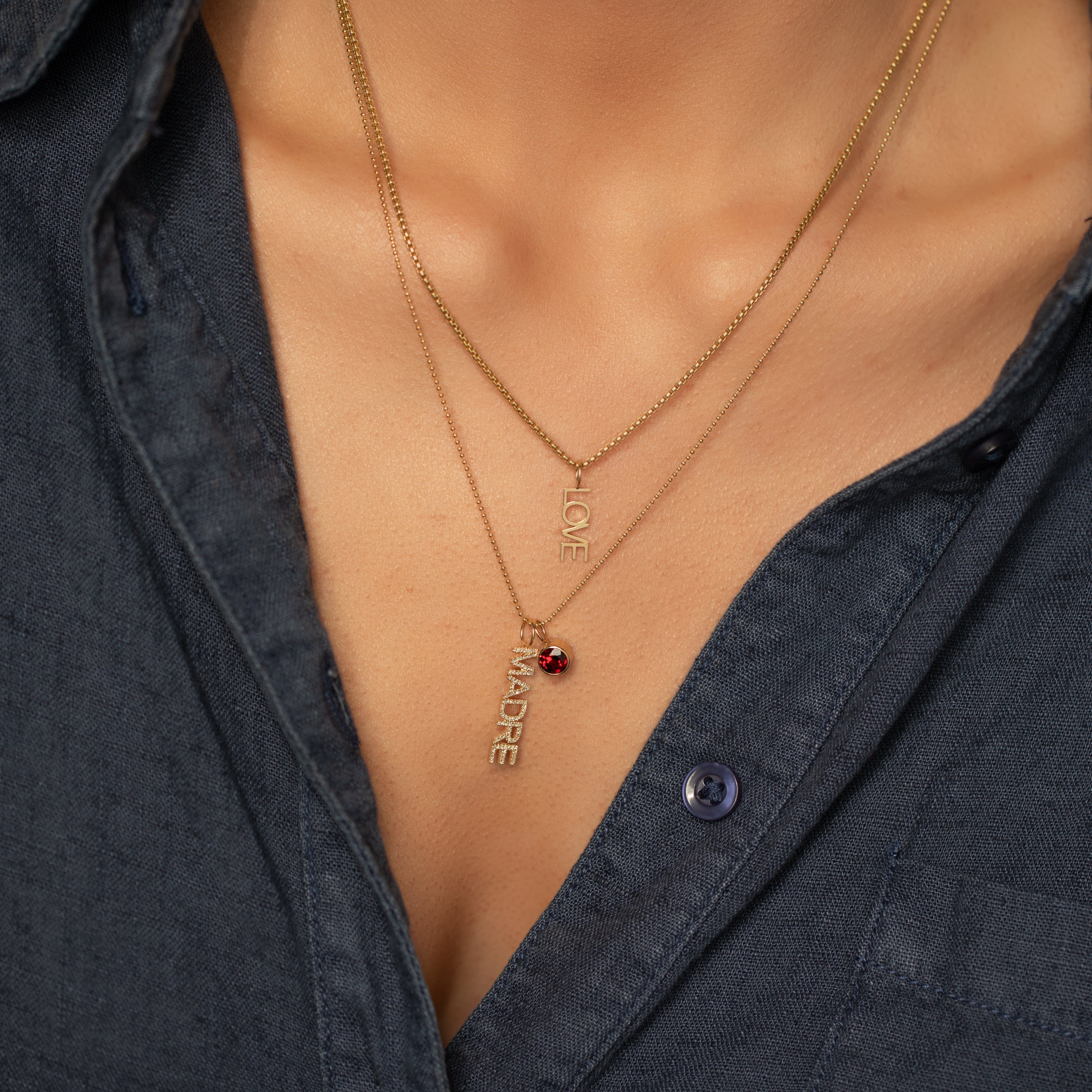 Necklaces with 'LOVE' and 'MADRE' pendants layered on a person wearing a dark shirt.