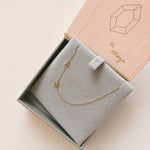 Gold necklace with 'A' and M' pendant in a jewelry box with 'xo Maya' branding.